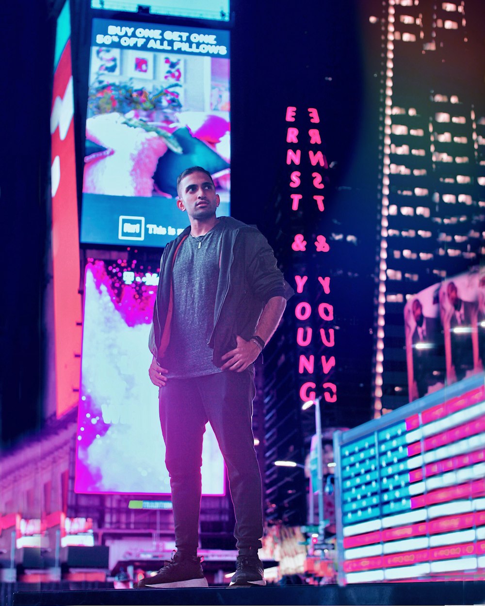 man in grey jacket and pants standing in front of electronic billboards