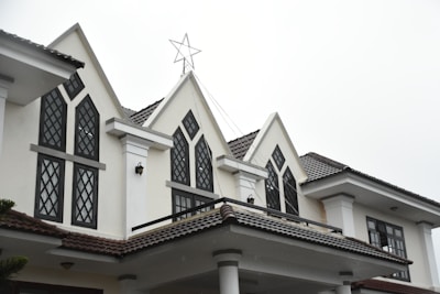 A white building with a complex architectural design featuring multiple peaked roofs and large, arched windows framed with dark grids. A prominent star decoration sits atop the center peak. The building's exterior includes decorative columns and a tiled roof.