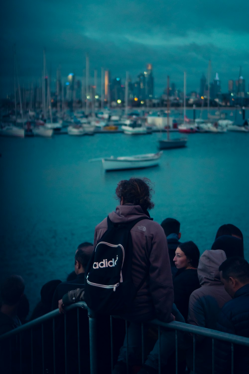 gente de pie y mirando en el mar en calma con la línea de los barcos