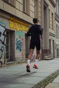 man in black shorts and shirt jogging at sidewalk