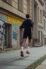 man in black shorts and shirt jogging at sidewalk