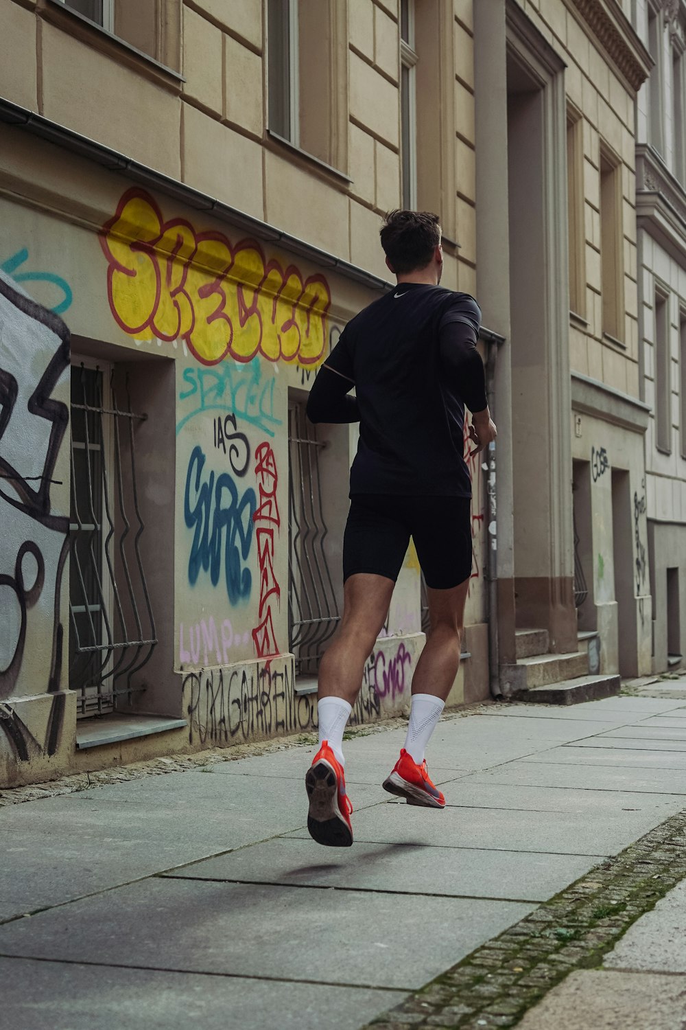 uomo in pantaloncini neri e camicia che fa jogging sul marciapiede