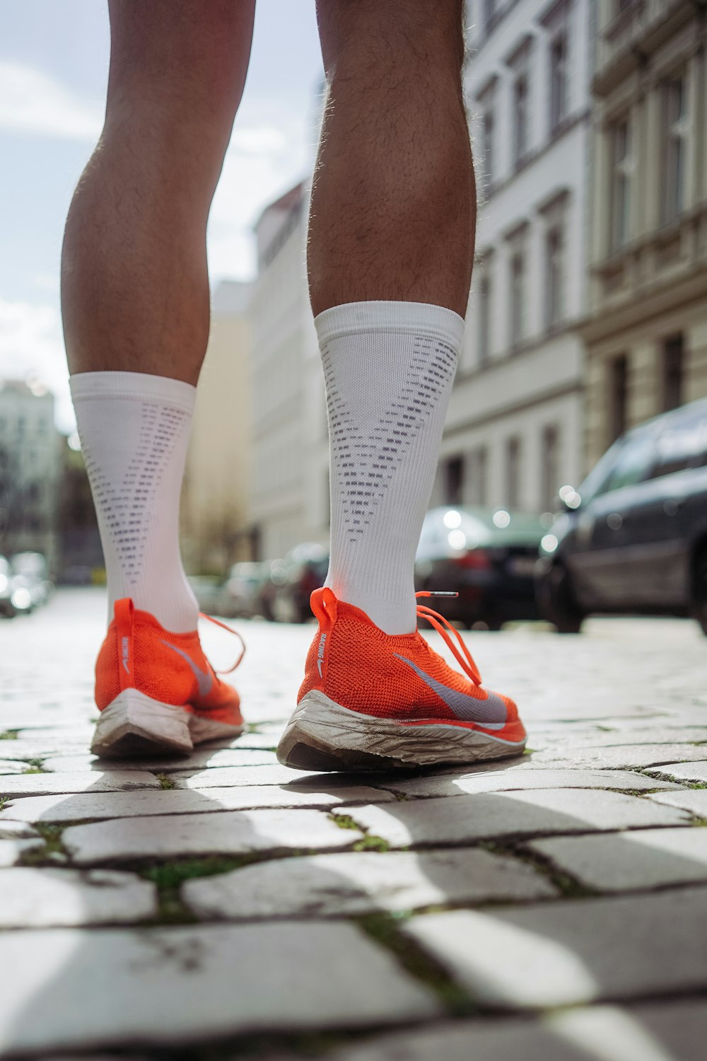 Person mit orangefarbenen Nike-Laufschuhen, die auf dem Bürgersteig steht