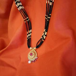 Close-up of a delicate black bead mangalsutra with gold pendant resting on a silk fabric