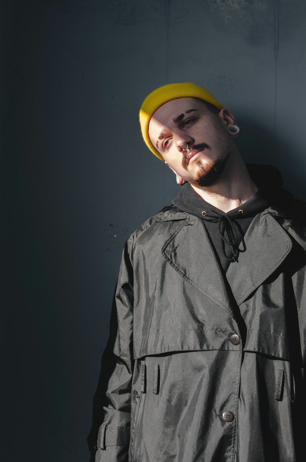 man wearing black coat and yellow beanie leaning on the wall