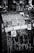 A black and white urban scene featuring a public space covered with various stickers and graffiti. The stickers include QR codes, warning labels, and artistic designs, layered over a backdrop of chaotic spray paint and marker scribblings.