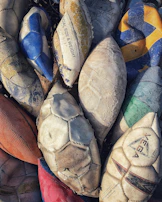 A collection of sports balls including basketballs, soccer balls, and volleyballs stacked together.