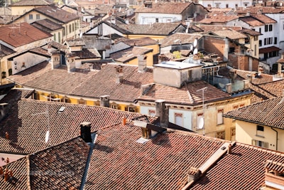 A dense cluster of old buildings with red-tiled roofs, tightly packed together. The rooftops are predominantly red and brown, and various architectural styles are visible, with some buildings showcasing stucco and others brick exteriors. Chimneys and satellite dishes are scattered throughout the scene.