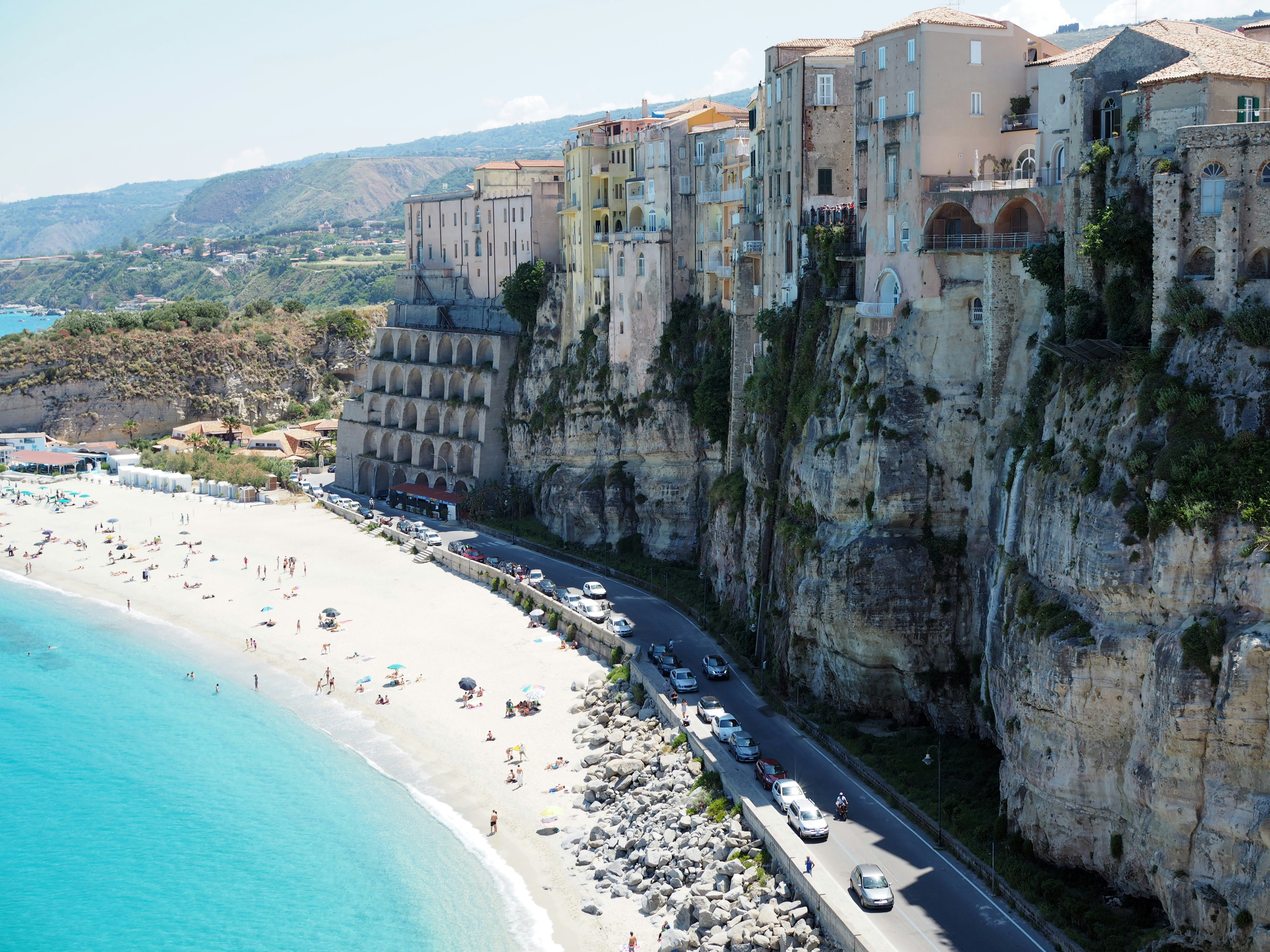 cars passing on highway between beach and houses on cliff