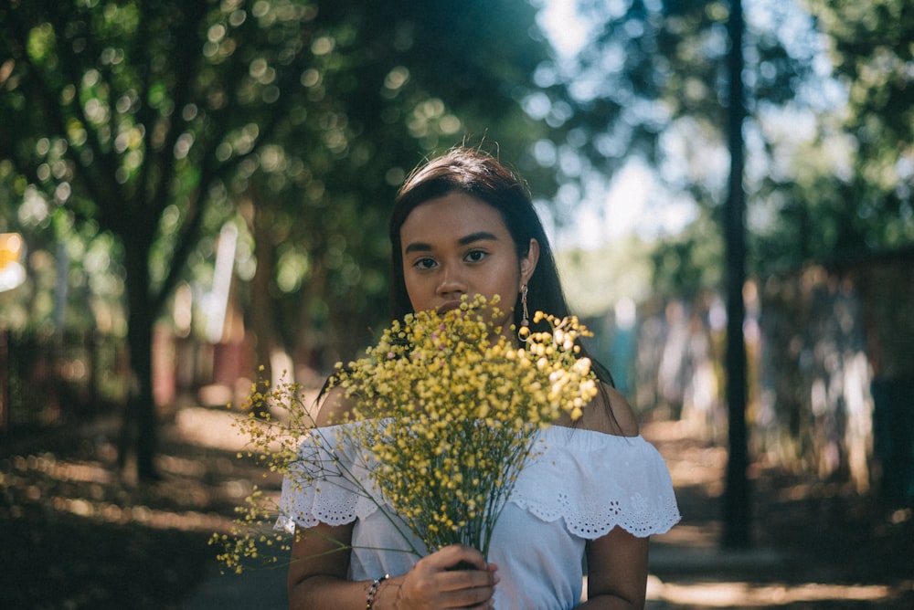 woman wearing white blouse holding yellow flowers