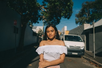 A young woman wearing a loose, oversized Catholic-themed t-shirt standing in a sunlit urban street.