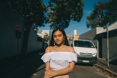 A young woman wearing a loose, oversized Catholic-themed t-shirt standing in a sunlit urban street.
