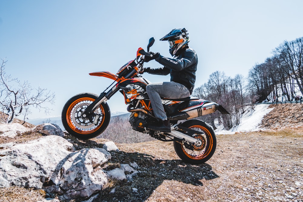 man riding orange and black dirt bike during daytime