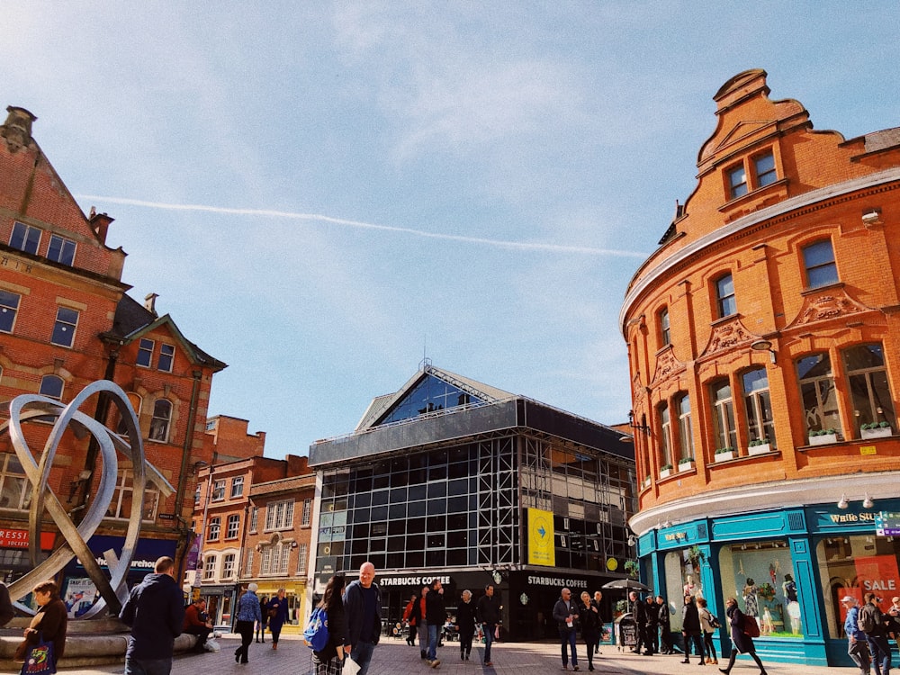 people walking beside buildings under cloudy sky with contrail