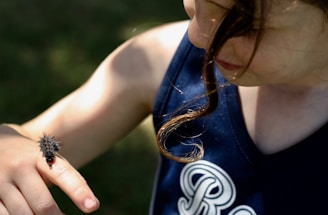 A young person curiously observes a spiky caterpillar resting on their finger, with sunlight highlighting their features and casting shadows.