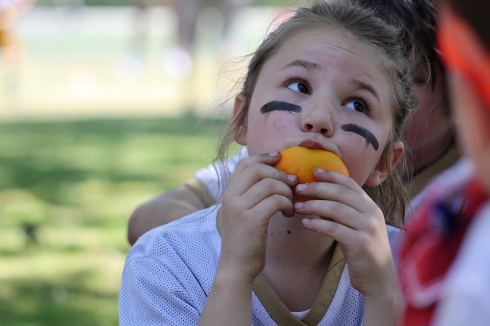 girl eating orange during daytime