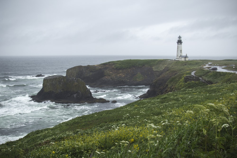 white and black lighthouse on cliff under cloudy sky during daytime