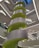 A modern interior structure featuring a large spiral staircase with bright green accents and sleek gray panels. The architecture displays clean lines and geometric forms, with multiple levels visible. Overhead lighting casts a neutral glow throughout the space.