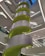 A modern interior structure featuring a large spiral staircase with bright green accents and sleek gray panels. The architecture displays clean lines and geometric forms, with multiple levels visible. Overhead lighting casts a neutral glow throughout the space.