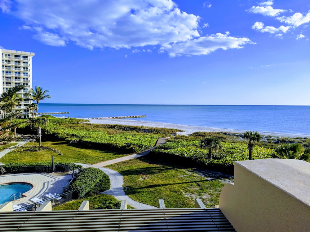 white concrete hotels and building near green field viewing calm sea under white and blue skies