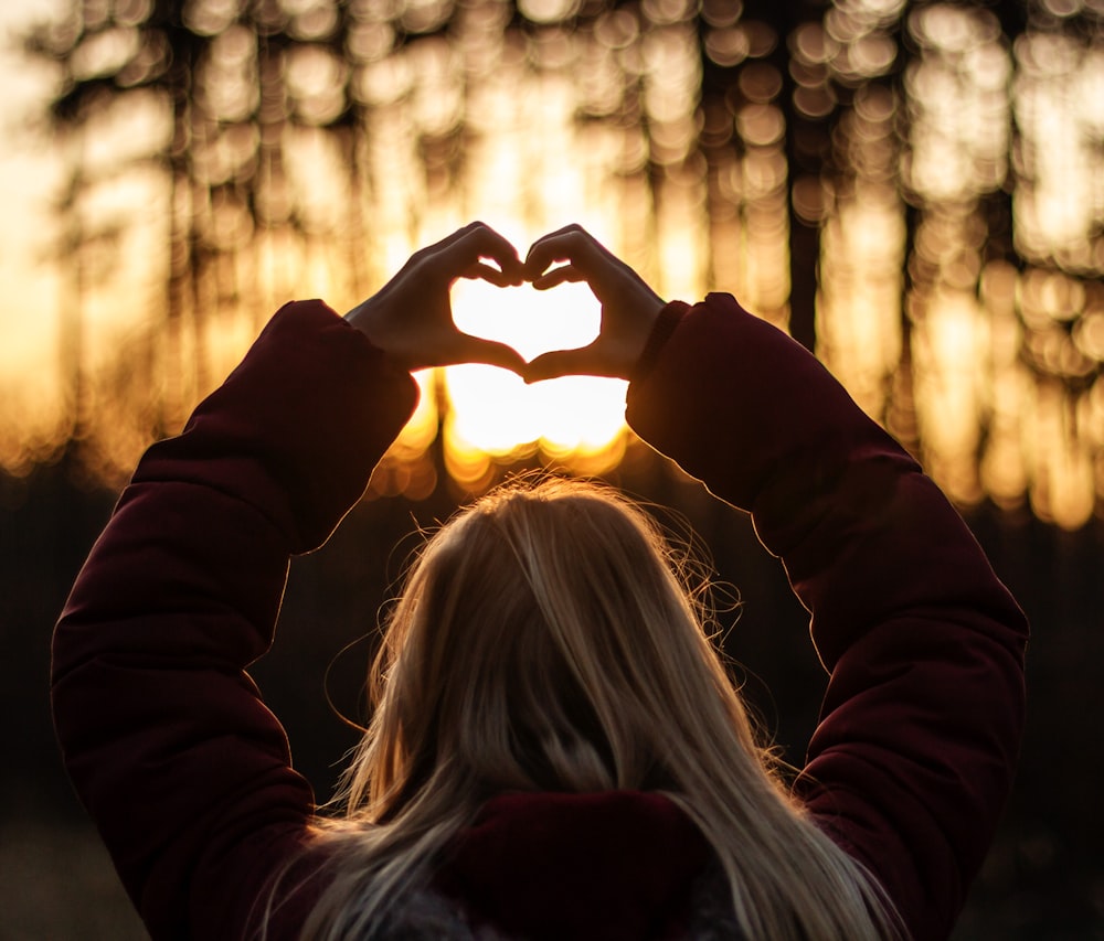 selective focus photography of woman doing heart hand sign