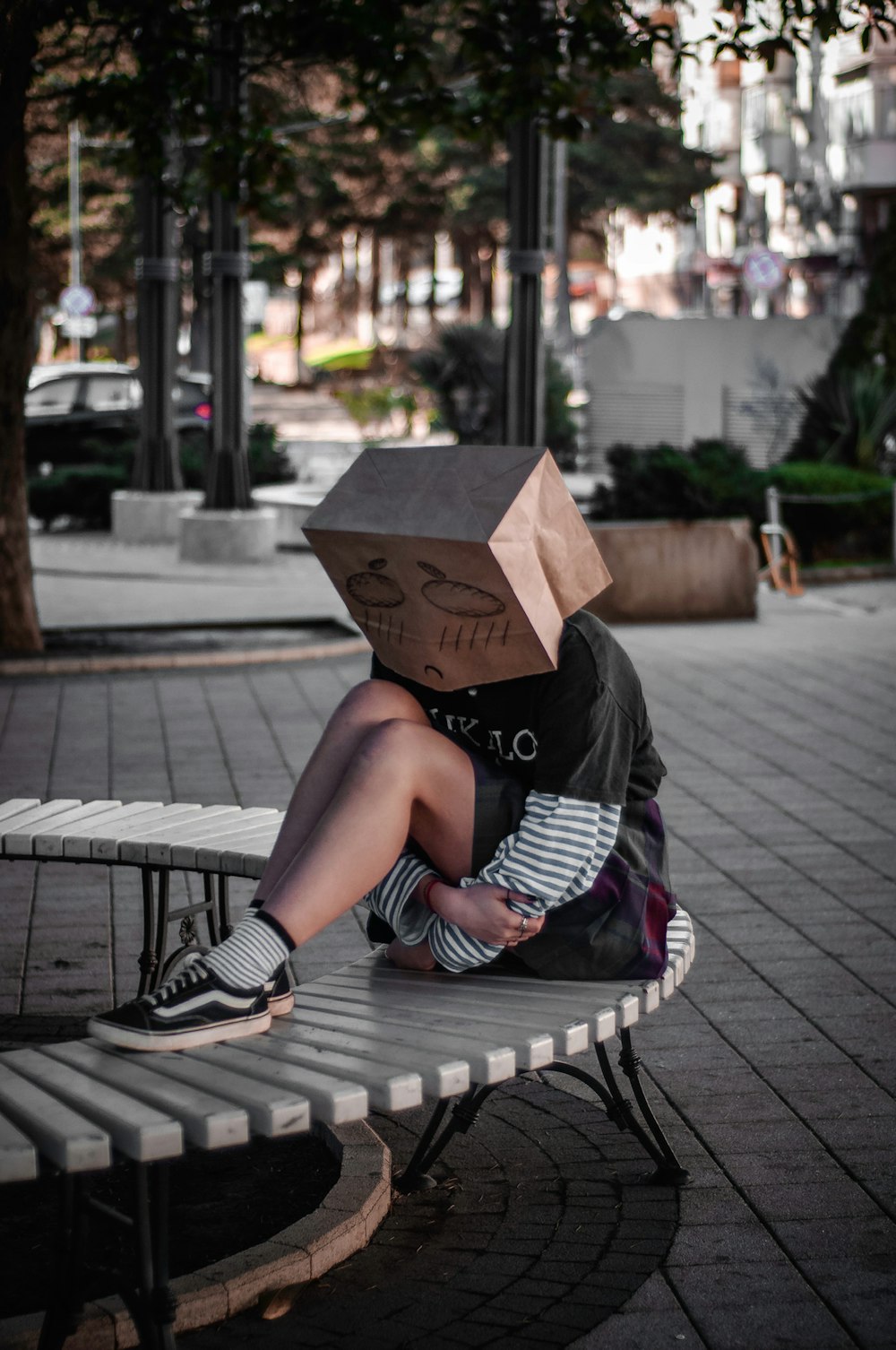 woman sitting on bench with paper bag on face