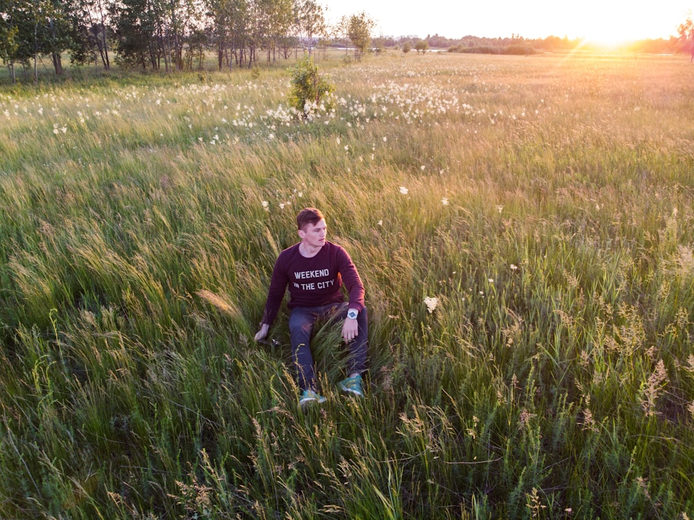 uomo in maglione nero che si siede sul campo di erba verde