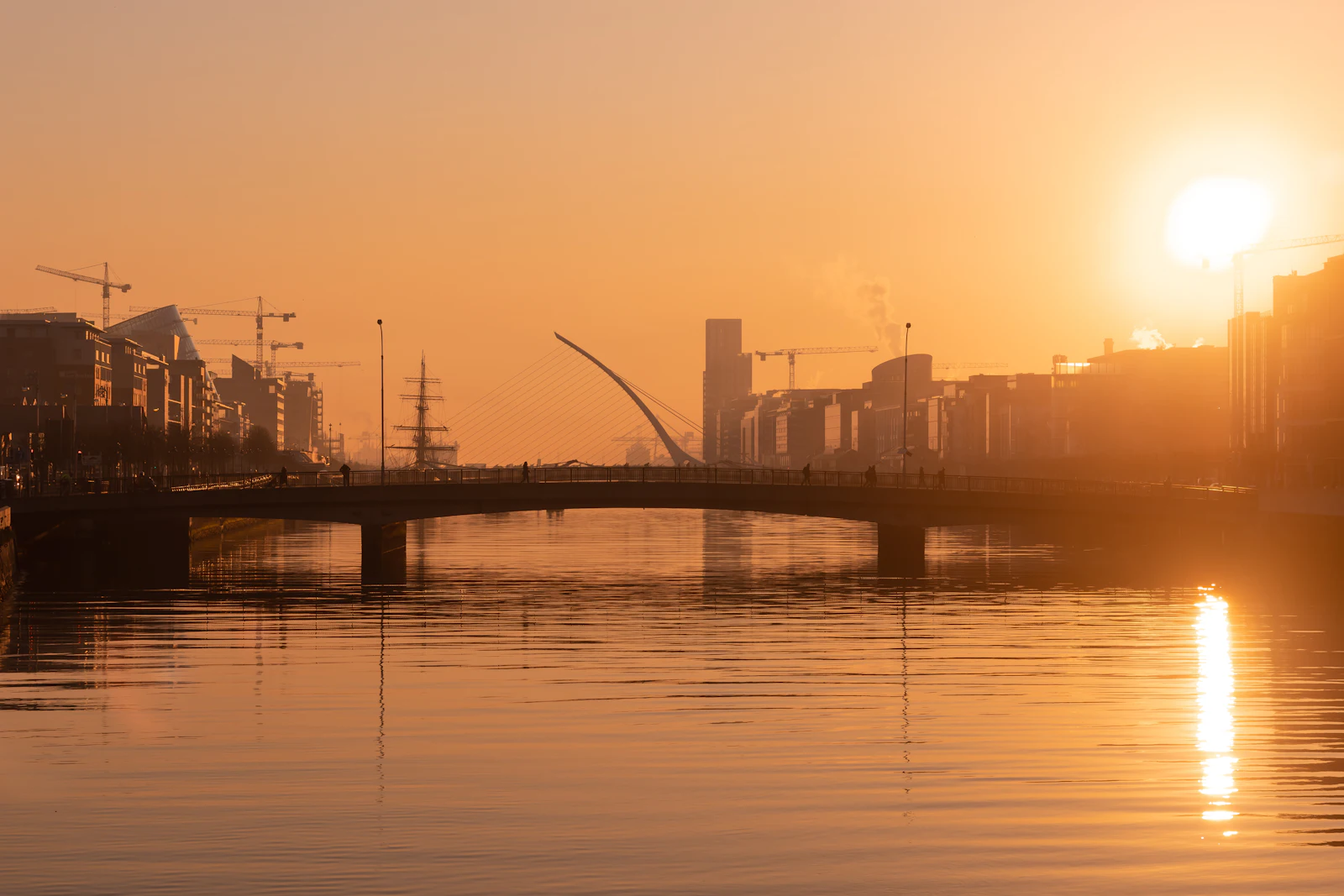 The River Liffey in Dublin at golden hour with the Samuel Beckett Bridge and docklands skyline, a city where an Ireland eSIM helps with transit apps