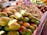 A market stall displaying an abundance of fresh, ripe mangoes piled on top of each other, with various other produce items like beans and pineapples visible in the background, all under a warm and natural light.