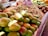 A market stall displaying an abundance of fresh, ripe mangoes piled on top of each other, with various other produce items like beans and pineapples visible in the background, all under a warm and natural light.