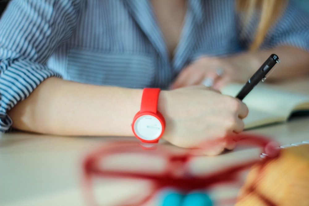 person wearing red analog watch holding twist pen