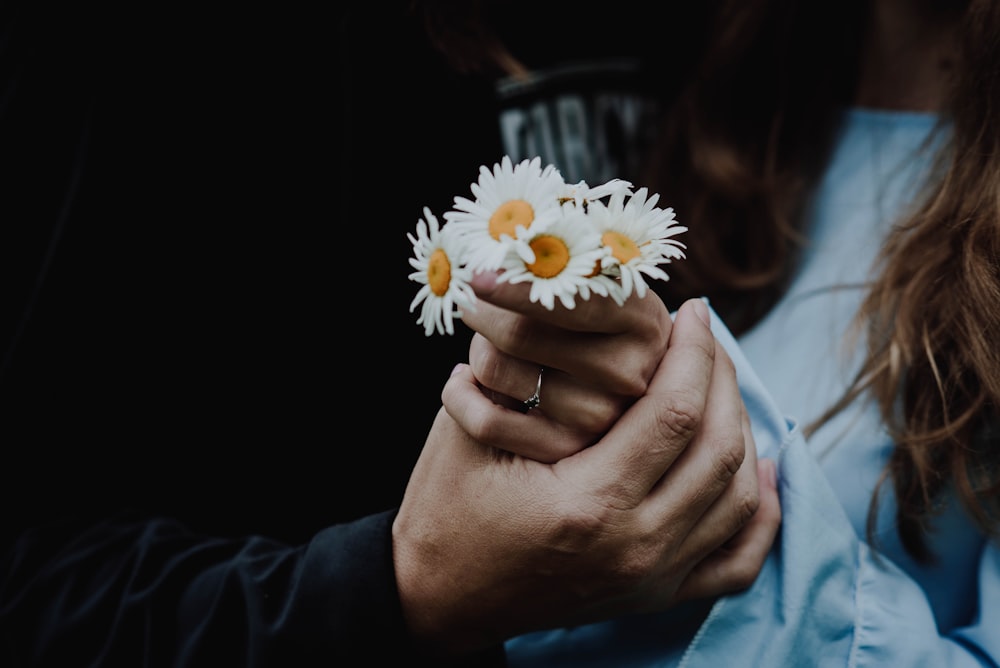 low-light photo of man holding the hand of woman holding white daisies