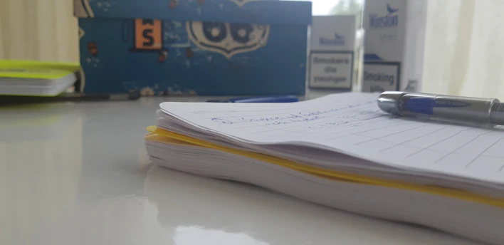 A close-up of a sleek journal page with handwritten habit notes and a blue pen resting on a clean white desk.