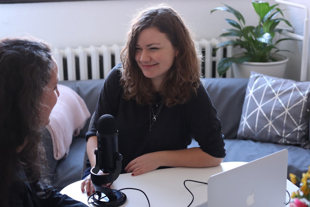 woman in black half-sleeved shirt sitting while facing woman and smiling