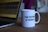 A white ceramic mug featuring the slogan 'THE FUTURE IS FEMALE' is placed on a wooden table. There is a visible lipstick mark on the rim of the mug. Beside the mug, part of an open laptop is visible, displaying what appears to be soundwave patterns on the screen.