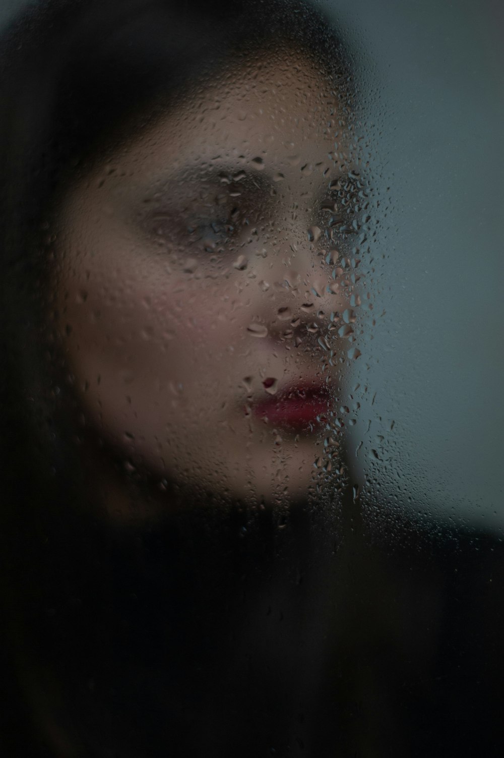 湿ったガラス窓の後ろの女性
