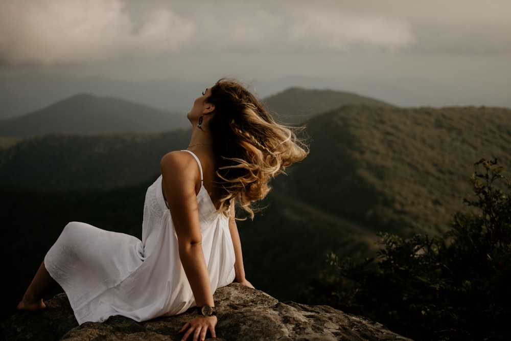 언덕에 앉아있는 흰색 민소매 드레스를 입은 여자