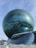 A modern architectural structure with a large spherical glass building. Reflective surfaces show the surrounding environment, and the structure sits under a clear blue sky. The architecture blends futuristic design with geometric patterns.