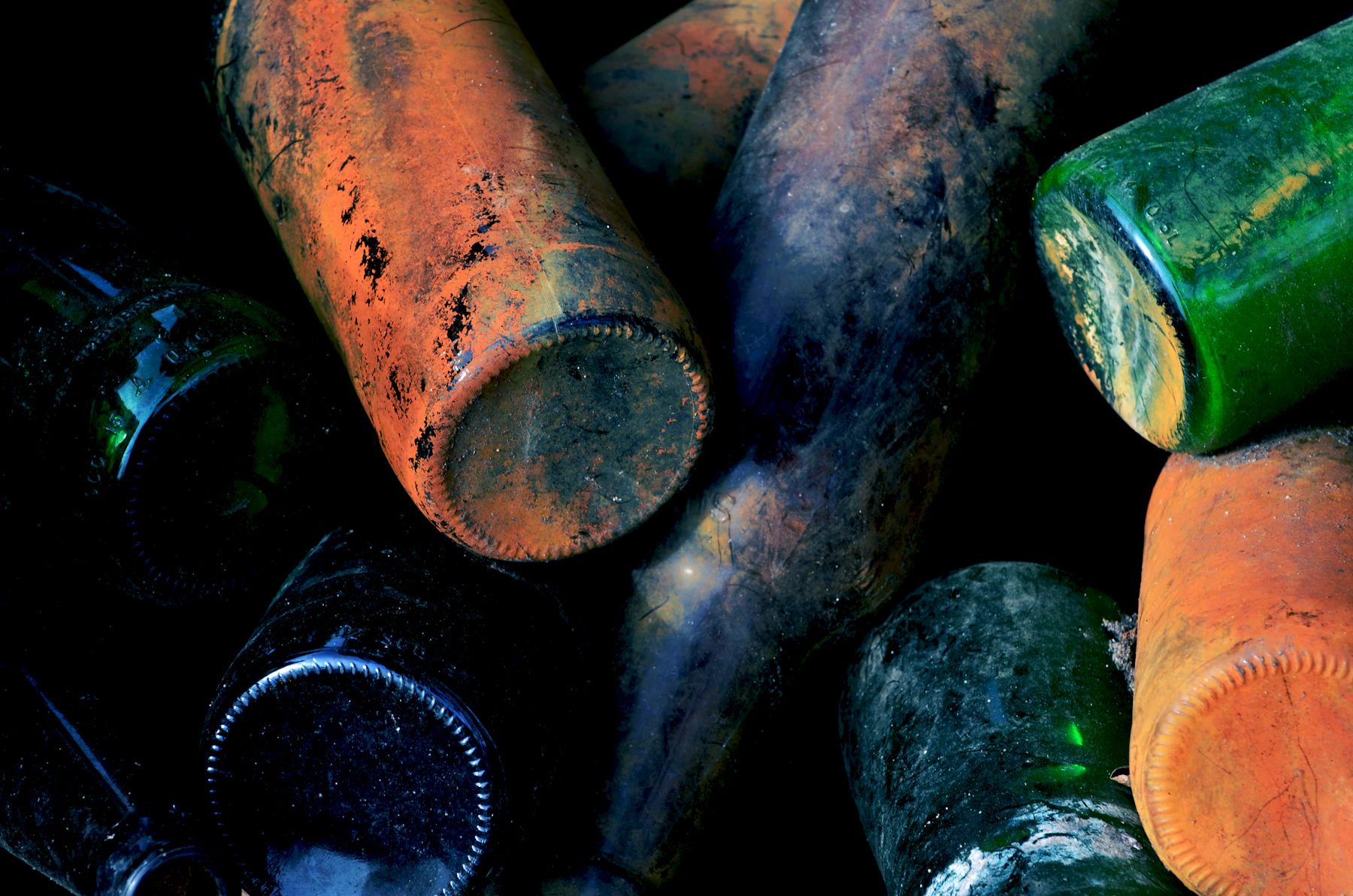 Dirt-crusted old bottles lying in a pile with their bases toward the camera