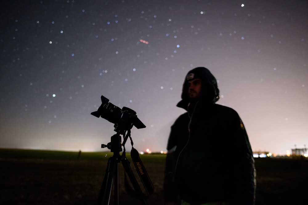 man standing beside telescope with tripod
