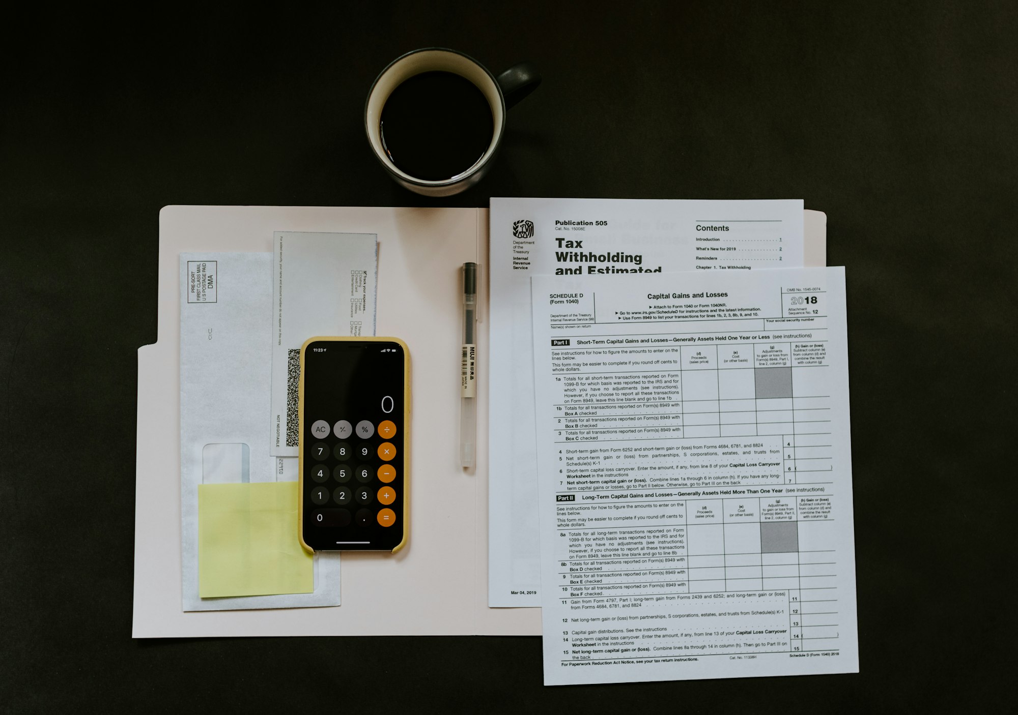 Téléphone avec l'application calculette posée sur une chemise contenant des documents et un stylo, avec une tasse 