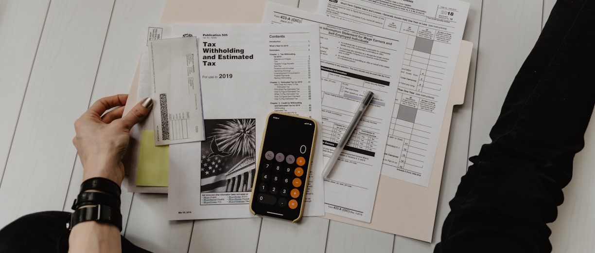 person holding paper near pen and calculator