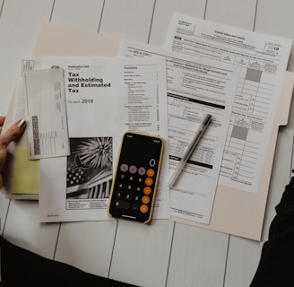 person holding paper near pen and calculator