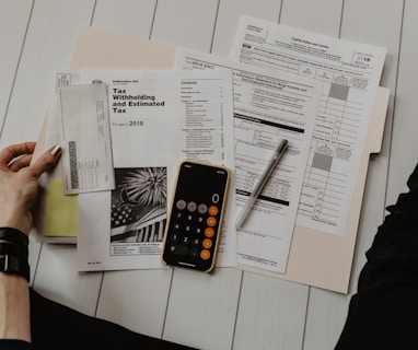 person holding paper near pen and calculator