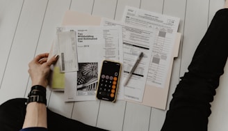 A person sitting on the floor with financial documents, a phone calculator, and a pen