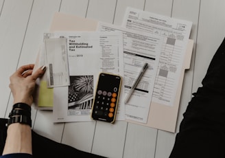 person holding paper near pen and calculator