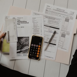 person holding paper near pen and calculator