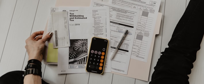 person holding paper near pen and calculator