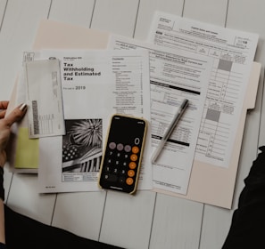 person holding paper near pen and calculator