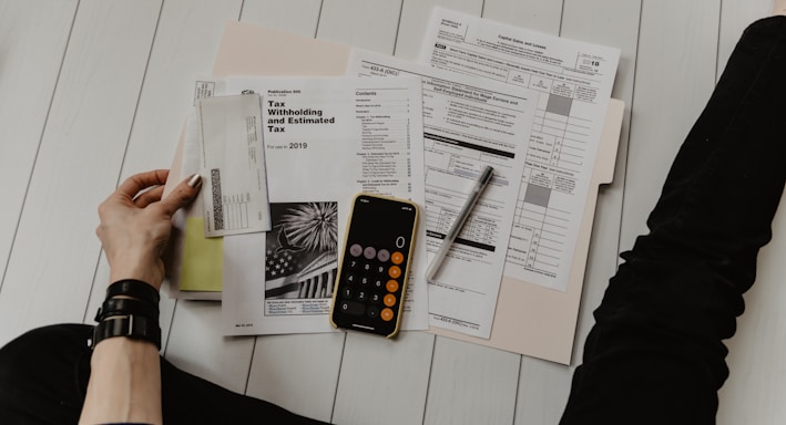 person holding paper near pen and calculator